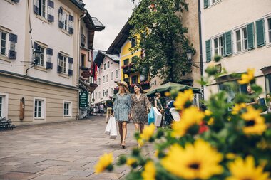Pedestrians exploring the picturesque pedestrian street in Zell am See with colorful buildings and flowers in the foreground. | © Zell am See-Kaprun Tourismus